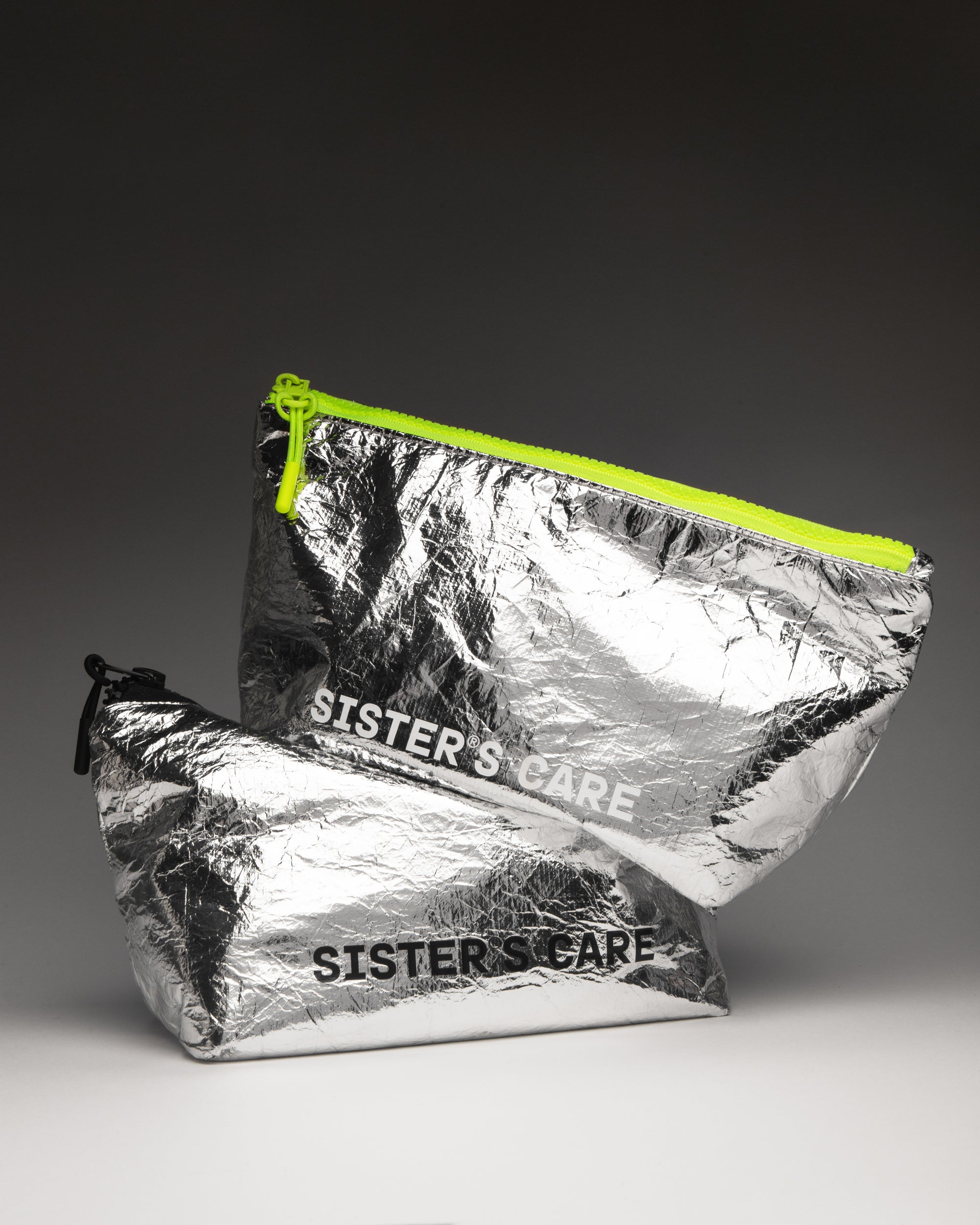Sister's Aroma Cosmetic bags in shiny silver with neon zip, perfect for stylish beauty on the go.
