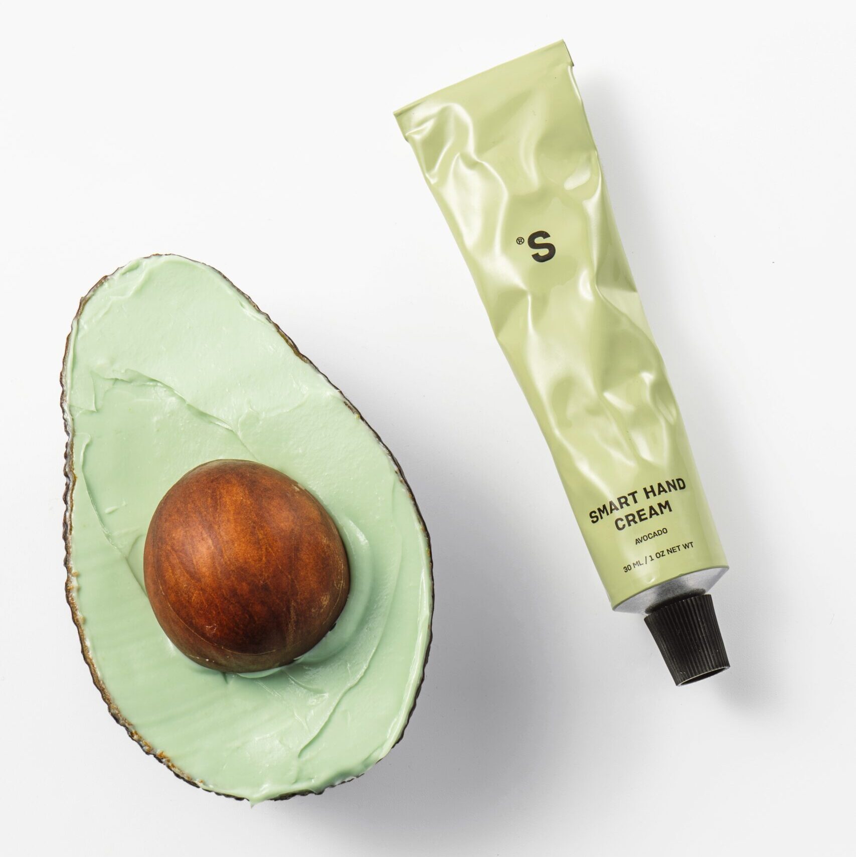 Sister's Aroma Smart Hand Cream in green tube next to halved avocado, showcasing hydrating skincare.