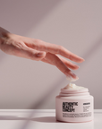 Hand reaching for Authentic Beauty Concept Glow Mask jar, showcasing its creamy texture and stylish packaging.