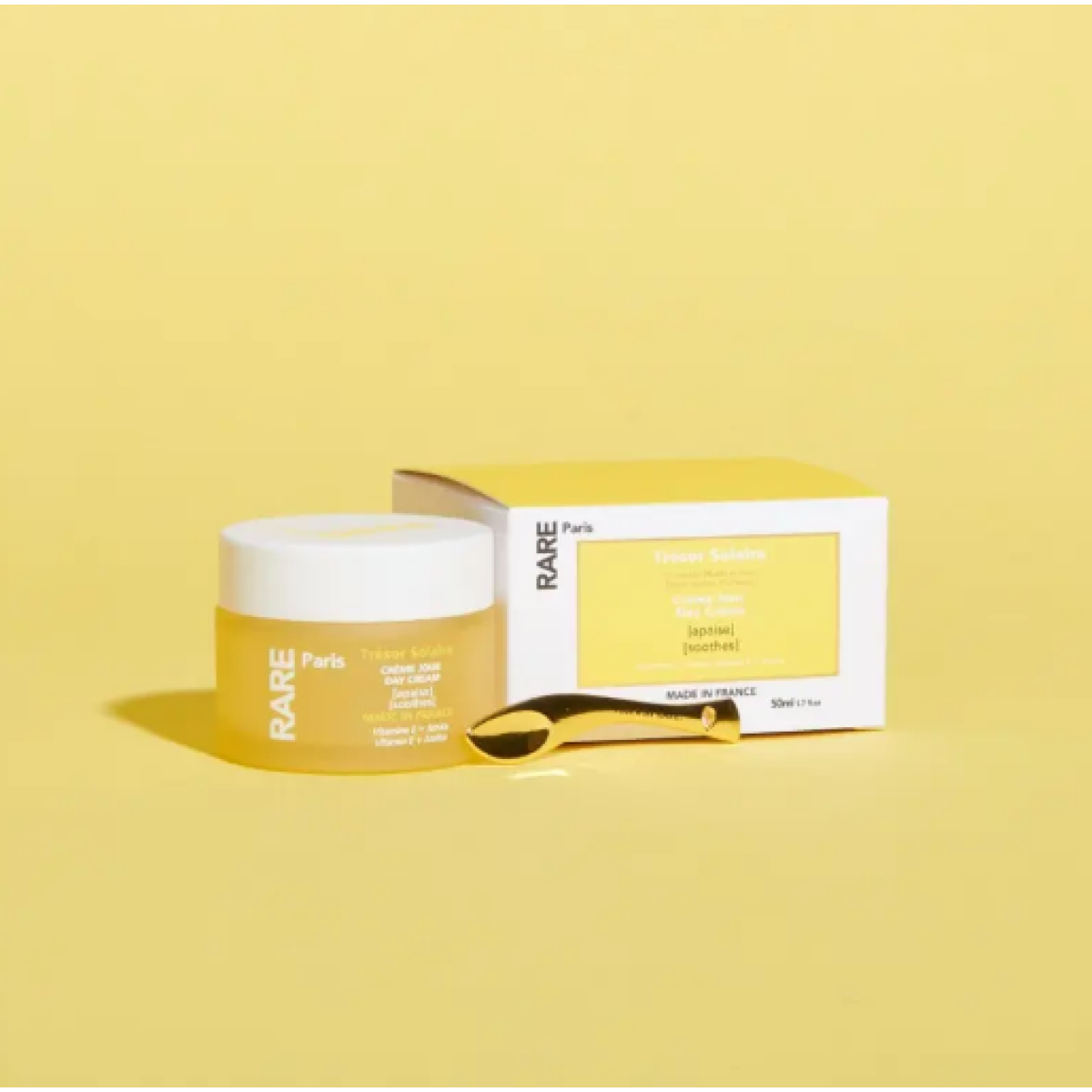 Rare Paris Trésor Solaire Day Cream jar and box on a bright yellow background, featuring soothing ingredients for sensitive skin.
