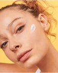 woman applying Rare Paris Trésor Solaire Day Cream on her face against a yellow background