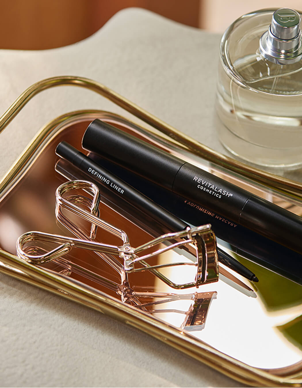 RevitaLash Signature Eyelash Curler Kleštičky na řasy alongside defining liner and cosmetics on a stylish tray.